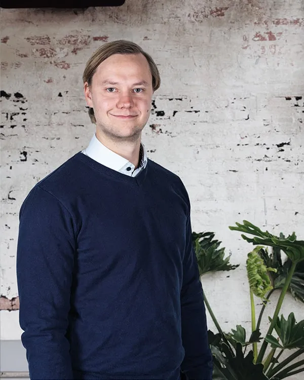 Fredrik Eklund in a navy sweater and white collar, in front of a whitewashed brick wall.